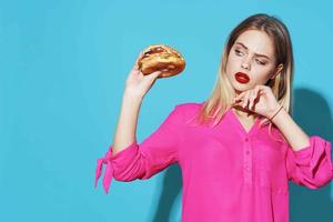 allegro bionda nel un' rosa camicia Hamburger veloce cibo merenda blu sfondo foto