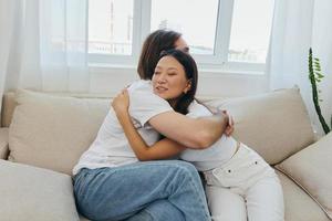 un' uomo e un' donna siamo seduta su il divano a casa indossare bianca magliette e abbracciare ogni altro con sorrisi. famiglia vita stili di vita di giovane sposati foto