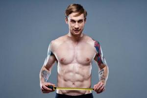 carino atleta con centimetro nastro fitness modello bodybuilder tatuaggio su il suo braccio grigio sfondo foto