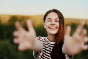 un' donna sorrisi e tira sua mani per il telecamera avvicinamento nel natura con un' Visualizza di il montagne. contento viaggio stile di vita Seguire me foto