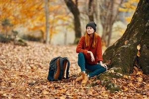 donna vicino albero e zaino per viaggio caduto le foglie autunno foresta foto