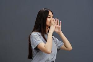 ritratto donna con lungo capelli nel un' grigio maglietta Esprimere a gesti con mani grigio sfondo foto