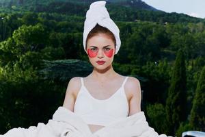 attraente giovane donna con un' asciugamano su il suo testa cerotti su il suo viso sta su il balcone guardare su il Visualizza foto