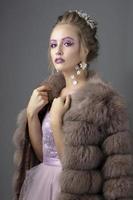 bellissimo modello con alla moda trucco nel un' pelliccia cappotto. lusso inverno ragazza su un' grigio sfondo. foto