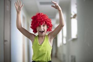 un' bambino nel un' luminosa parrucca. divertente ragazzo con rosso artificiale capelli. artista scolaro foto