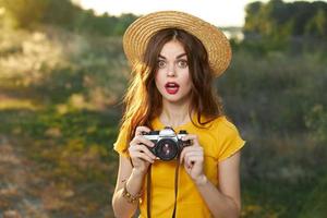 innamorato donna Tenere un' telecamera nel sua mani cappello rosso labbra giallo maglietta fresco aria foto