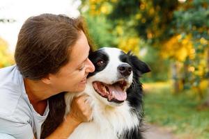 sorridente giovane donna attraente che gioca con un simpatico cucciolo di cane border collie su sfondo estivo all'aperto. ragazza che tiene abbracciando che abbraccia amico cane. concetto di cura degli animali e animali. foto