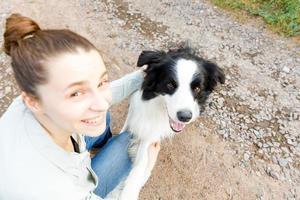 sorridente giovane donna attraente che gioca con un simpatico cucciolo di cane border collie su sfondo estivo all'aperto. ragazza che tiene abbracciando che abbraccia amico cane. concetto di cura degli animali e animali. foto