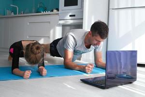 padre e figlia siamo esercizio, fare il tavola mentre guardare a il il computer portatile. il famiglia giochi gli sport in linea a casa. famiglia giochi gli sport durante il covid-19 pandemia foto