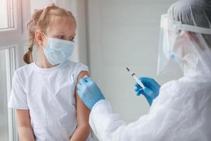 un' medico nel un' protettivo completo da uomo fa il bambino nel un' medico maschera un' spalla tiro . coronavirus vaccinazione. covid-19 vaccino. medico vaccinazione bambino. bambini a clinica. foto