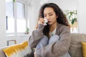 infelice giovane asiatico donna pianto solo vicino su, depresso ragazza seduta su divano a casa, Salute problema o pensiero di cattivo relazioni, rompere su con fidanzato, divorzio foto