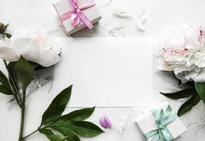 peonie rosa con una carta vuota e una confezione regalo su uno sfondo bianco foto