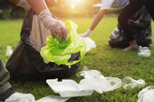 Due persone conservazione spazzatura plastica bottiglia in nero Borsa a parco nel mattina leggero foto