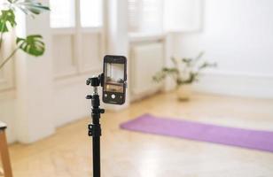 mobile Telefono su tripode nel vuoto vivente camera con fitness stuoie su il pavimento foto