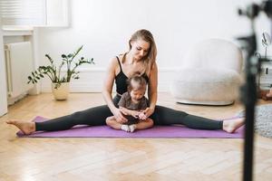 giovane donna con poco figlia fitness blogger fare esercizi e registrazione video su mobile Telefono nel studio foto