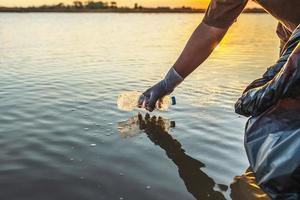 persone volontario conservazione spazzatura plastica bottiglia in nero Borsa su fiume nel tramonto foto