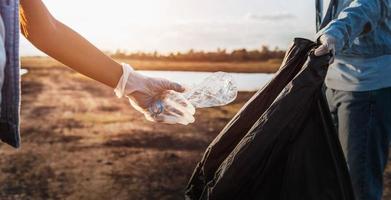 persone volontario conservazione spazzatura plastica bottiglia in nero Borsa a parco vicino fiume nel tramonto foto