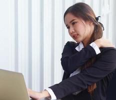 donna asiatica in ufficio ha dolore a causa di lunghe ore di seduta foto