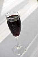 piccolo bicchiere di vino rosso su uno sfondo bianco con le ombre