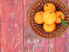 arance in una ciotola di vimini su uno sfondo di tavolo in legno foto