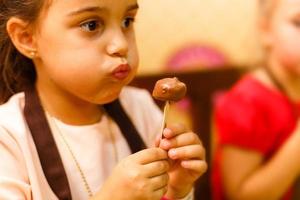 un' poco ragazza mangiare cioccolato marshmallow fonduta su un' bastone. foto