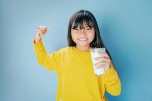 carino litle ragazza potabile latte nel bicchiere con sorridente contento su blu sfondo foto