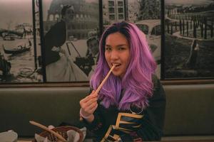 viola capelli asiatico donna mangiare un' grissino a il italiano ristorante foto