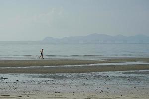 salutare uomo corre solo lungo il spiaggia con orizzontale linea di paesaggio marino nel sfondo foto