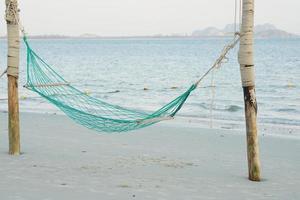 vuoto swing intrecciato di corda sospeso su il di legno poli su il spiaggia con paesaggio marino sfondo foto