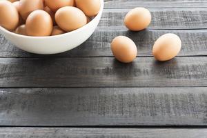 uova di gallina in una ciotola bianca e tre uova di gallina fuori su un tavolo di legno nero foto