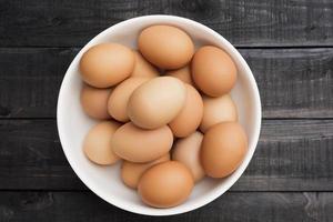 uova di gallina fresche in una ciotola bianca su un tavolo di legno nero foto