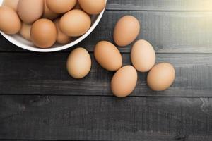 uova di gallina fresche in una ciotola bianca e sei uova fuori su un tavolo di legno nero foto