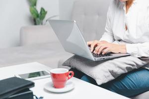 sociale media giorno concetto. femmina libero professionista di partenza Lavorando giorno presto nel mattina potabile caffè nel vivente camera per sito web con utilizzando moderno il computer portatile computer. donna d'affari Lavorando nel casa ufficio. foto