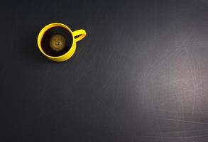 giallo tazza di caffè nero piatto giaceva su sfondo nero ruvido graffiato foto