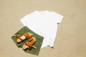 sabbia spiaggia struttura sfondo. modello bianca estate maglietta copia spazio. vuoto modello donna camicia superiore Visualizza. estate Accessori jeans, sandali. piatto-lay avvicinamento maglietta spiaggia. tempo di spiaggia foto