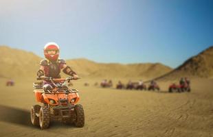 poco ragazza equitazione atv quadrilatero bicicletta nel deserto con bellissimo blu e bianca cielo . foto