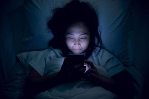 asiatico donna giocando gioco su smartphone nel il letto a notte, Tailandia persone, tossicodipendenti sociale media foto