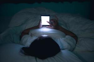 asiatico donna giocando gioco su smartphone nel il letto a notte, Tailandia persone, tossicodipendenti sociale media foto