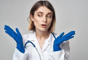 un' infermiera nel un' medico toga e blu guanti gesti con un' stetoscopio in giro sua collo foto