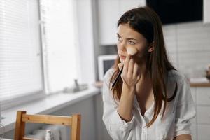 bellissimo donna con trucco spazzola a il tavolo nel il cucina foto