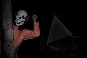 asiatico bello uomo indossare clown maschera con arma a il notte scena, halloween Festival concetto, orrore pauroso foto di un' uccisore nel arancia stoffa