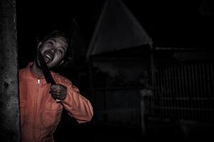 asiatico bello uomo indossare clown maschera con arma a il notte scena, halloween Festival concetto, orrore pauroso foto di un' uccisore nel arancia stoffa