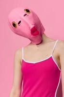 donna nel un' pesce costume per Halloween pose contro un' rosa sfondo nel un' pazzo pauroso costume con un' rosa silicone maschera su sua testa foto