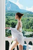 donna nel un' bianca camicia ammira il verde natura su il balcone stile di vita foto