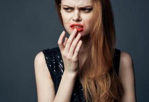 un' donna nel un' nero vestito con rosso labbra gesti con sua mani perplesso Guarda grigio sfondo foto