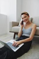 libero professionista donna con il computer portatile e Telefono lavori a partire dal casa seduta su il pavimento nel sua casa Abiti con un' corto taglio di capelli, gratuito copia spazio foto