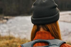 donna viaggiatore passeggiate nel natura nel il montagne vicino il fiume paesaggio modello cappello rosso capelli foto
