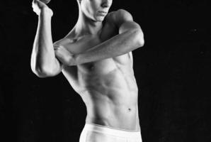 bodybuilder con un' pompato su corpo nel bianca mutandine in posa buio sfondo foto