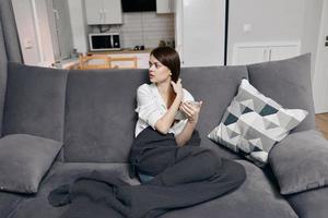 donna nel un appartamento con un' mobile Telefono seduta su il divano foto