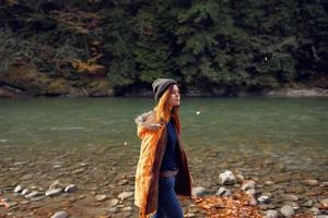 donna nel un' giallo giacca vicino il fiume ammira natura autunno foresta foto